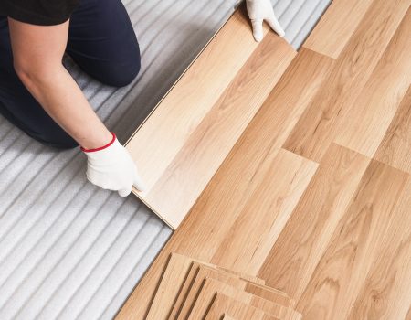 Installing laminated floor, detail on man hands holding wooden t Installing laminated floor, detail on man hands holding wooden tile, over white foam base layer