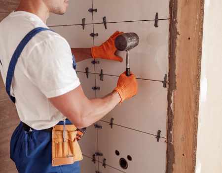 Male worker installing ceramic wall tile in house Close up of young man construction worker using rubber hammer while placing tile on the wall